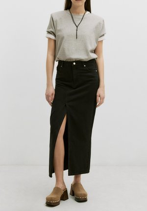 Zwarte denim maxi rok met een hoge split, gecombineerd met een grijs t-shirt. De outfit wordt aangevuld met bruine platformklompen met studs.