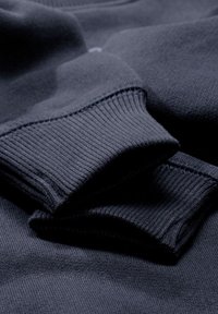 Tejido de suéter azul marino oscuro con puños acanalados, que presenta una textura suave y un detalle de costura sutil, mostrando un color uniforme y un caído suave.