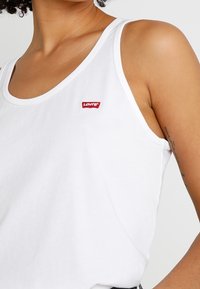 Hvid bomulds tanktop med rund halsudskæring og et lille rødt Levi's-logo på venstre bryst. Har brede stropper og en afslappet pasform.