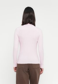 Lichtroze geribbelde longsleeve top met een getailleerd ontwerp, voorzien van een hoge hals en een geschulpte zoom, gecombineerd met een bruine broek.