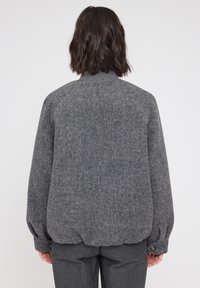 Gray wool jacket with a soft texture, rounded shoulders, and elastic hem. Features a button detail on sleeves and a high collar.