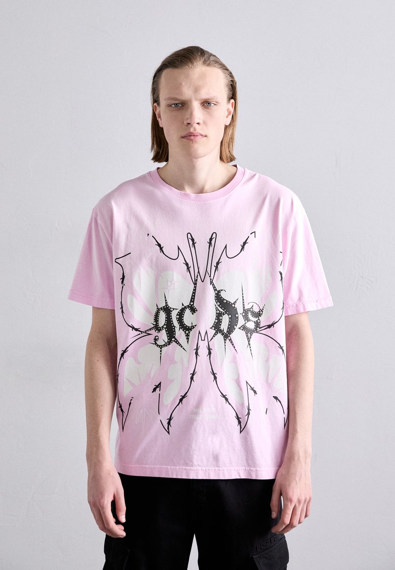 T-shirt en coton rose avec un grand motif de papillon noir et blanc, des accents pointus et du texte en police grasse. Manches courtes.