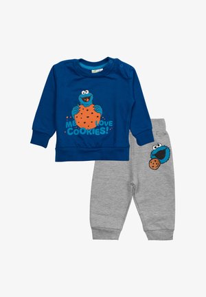Blauer Baumwoll-Sweatshirt mit Grafik des Keksmonsters, kombiniert mit grauen Baumwoll-Jogginghosen, die ein Keksdesign auf der Tasche haben.