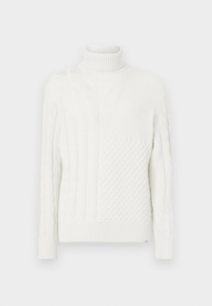 Hvid turtleneck sweater med blandede strikmønstre, herunder kabel- og vaffelmønstre, med lange ærmer og ribbede manchetter og kant.