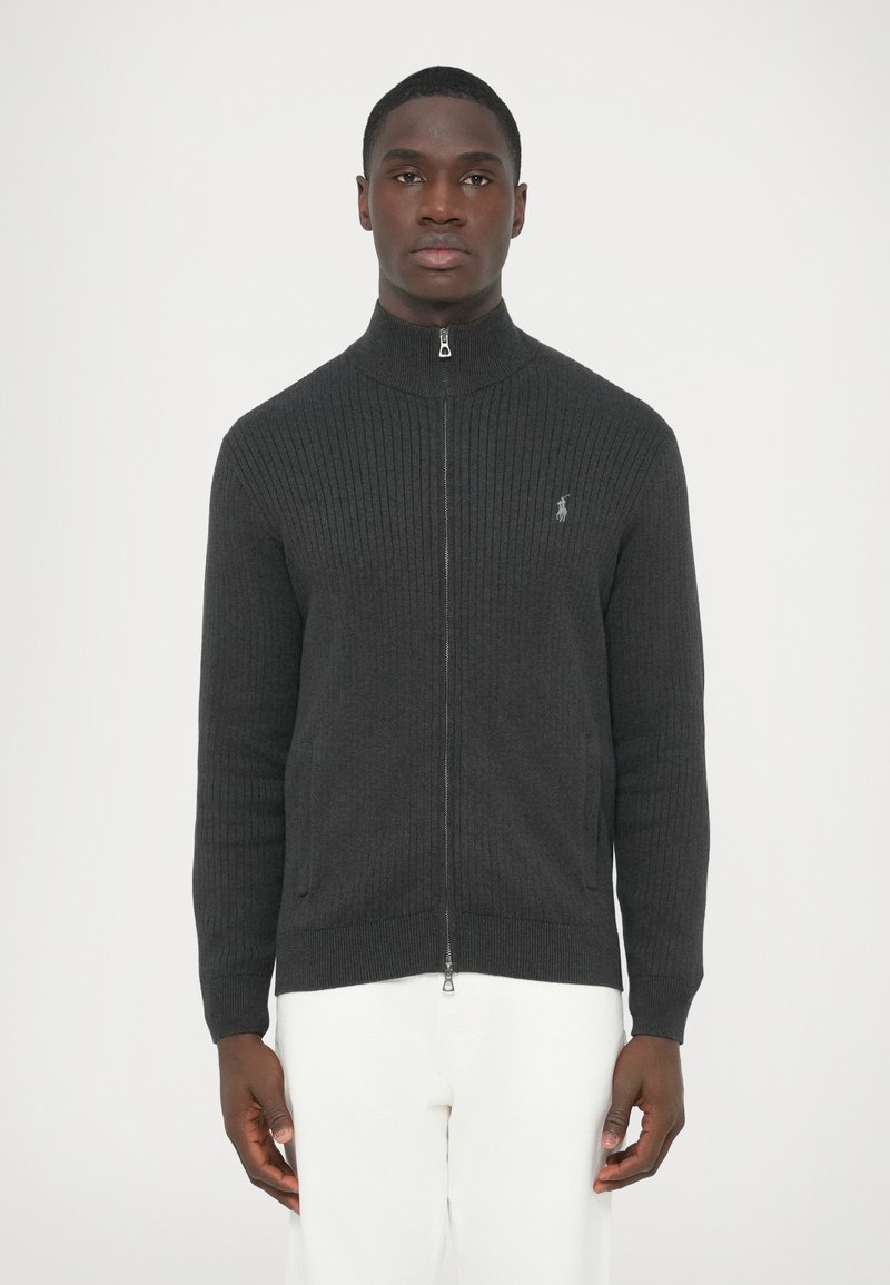 Sötétszürke bordázott cipzáras pulóver magas gallérral, két oldalzsebbel és egy kis hímzett logóval a bal mellrészen.