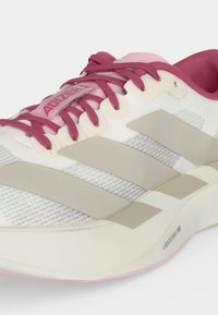 Λευκό και ροζ παπούτσι για τρέξιμο Adidas με μπορντό κορδόνια, μπεζ ρίγες και λεπτομέρεια στη σόλα "Lightstrike Pro", εμφανιζόμενο από πλάγια γωνία.