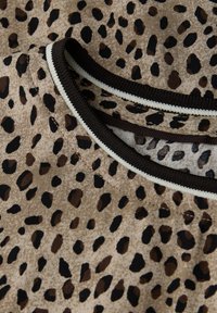 Il tessuto con stampa leopardata presenta sfumature di marrone e nero, con una superficie texture. Il collo ha un bordo in contrasto di marrone e crema.