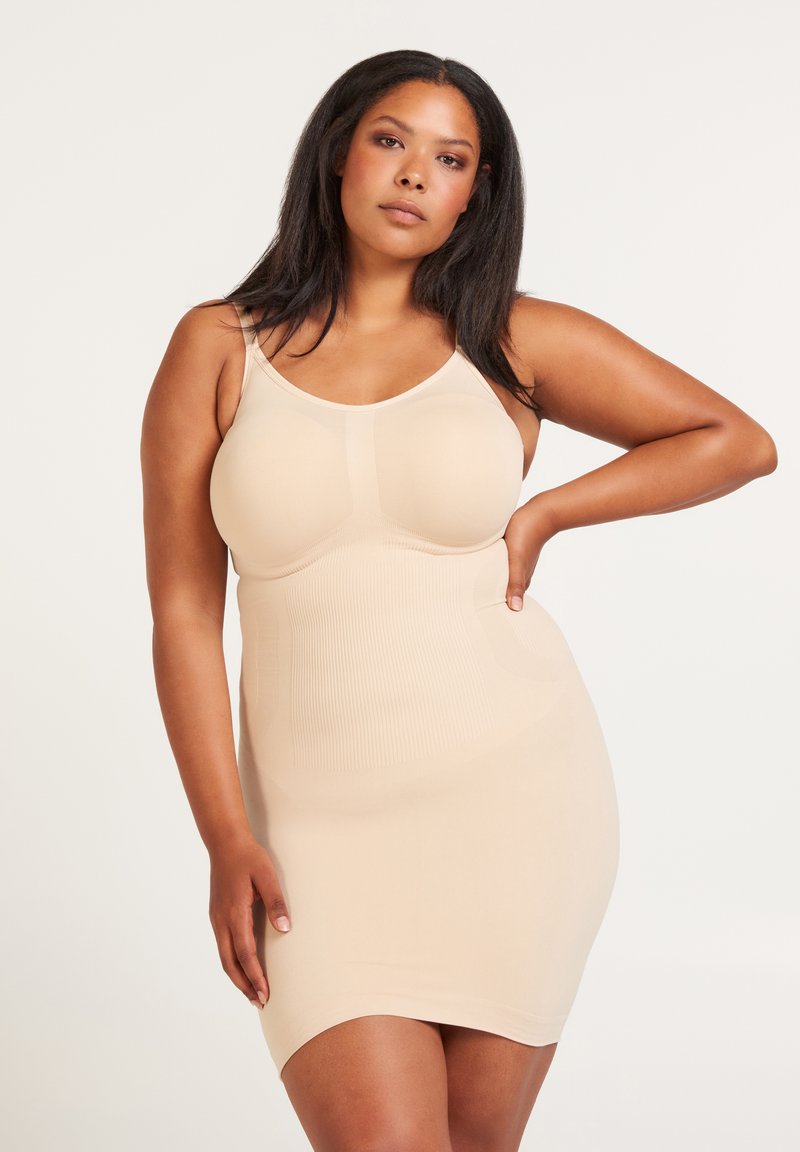 Beige shapewear-klänning med spaghettistappar, ribbat mönster, åtsittande design och formade kupor som ger en slät silhuett.