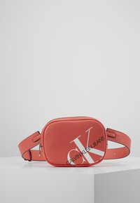 Borsa a tracolla rossa in ecopelle con forma rettangolare, caratterizzata da un audace logo bianco "CK" e una tracolla regolabile. Dettaglio della zip in argento visibile.