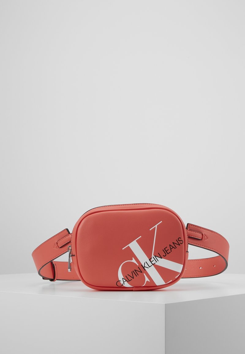 Borsa a tracolla rossa in ecopelle con forma rettangolare, caratterizzata da un audace logo bianco "CK" e una tracolla regolabile. Dettaglio della zip in argento visibile.