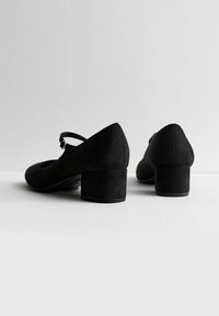 Zwart suede Mary Jane hakken met een ronde teen, korte blokhak en verstelbaar bandje met een gouden gespdetail.