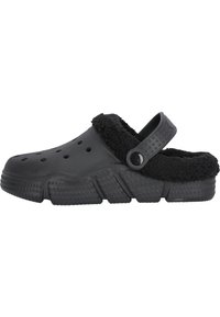 Chaussure de style sabot noir avec une doublure noire duveteuse, des trous de ventilation sur les côtés et une sangle arrière ajustable. Semelle texturée et ferme avec des zones surélevées.