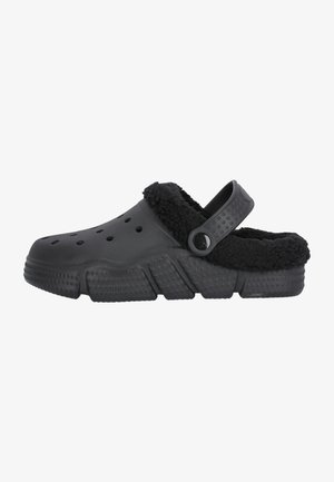 Chaussure de style sabot noir avec une doublure noire duveteuse, des trous de ventilation sur les côtés et une sangle arrière ajustable. Semelle texturée et ferme avec des zones surélevées.