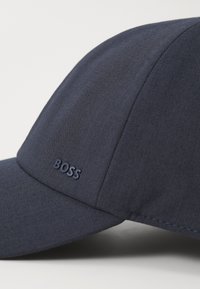 Navy modrá čepice s křivým břehem vyrobená z texturované tkaniny. Na přední levé straně se nachází embosované logo "BOSS".