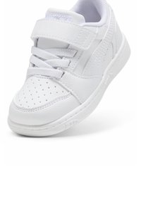 Bílé sportovní tenisky vyrobené z umělé kůže. Mají polstrovaný límec, perforovanou špičku, ploché tkaničky a suchý zip pro bezpečné uchycení.