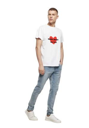 White cotton t-shirt features a red heart graphic with the text "make peace no war" in black. Paired with light blue jeans and white sneakers.