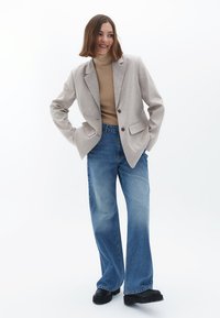 Helles graues Blazer mit zwei Knöpfen, beigem Rollkragenpullover und ausgewaschenen blauen weiten Jeans. Schwarze Plattformschuhe, glatte Textur, maßgeschneiderter Schnitt.