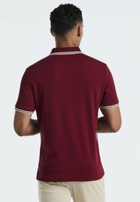 Bordeauxkleurig poloshirt met korte mouwen, voorzien van een gestreepte kraag en zijkanten in een contrasterend patroon. Soepele textuur, klassieke pasvorm.