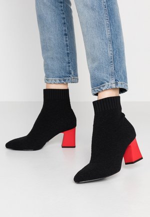 Bottines noires à cheville avec un revers côtelé et un talon bloc rouge contrastant. Bout pointu et tissu texturé complètent le design.