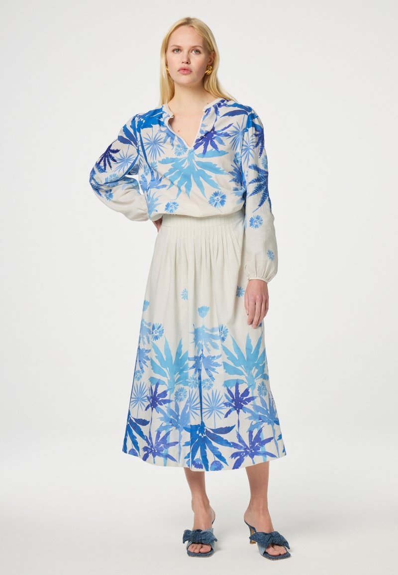 Blauw en witte bloemenprint blouse met lange mouwen, gecombineerd met een vloeiende witte rok met een verloop in blauw. Casual open teen schoeisel.