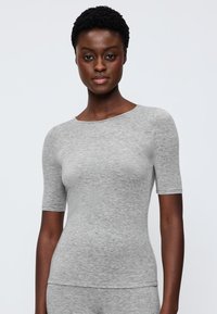 Top grigio a maniche corte realizzato in tessuto morbido con scollo rotondo. Presenta un design aderente e una superficie liscia. Il modello indossa il capo.