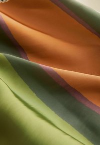 Tissu lisse avec de larges rayures horizontales dans des tons verts sourds, olive, violet et orange, plié délicatement pour mettre en valeur la texture et le contraste des couleurs.