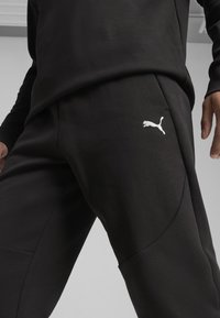 Svarta sweatpants av mjukt tyg, med en vit Puma-logotyp på vänster lår och rundade sidoseam för en modern design.