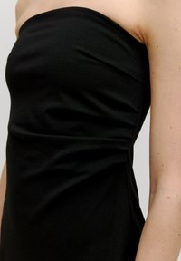 Schwarzes, trägerloses Kleid aus glattem Stoff, mit einem taillierten Oberteil und subtilen Drapierungselementen am Oberkörper.