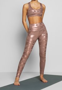 Conjunto de ropa activa en camuflaje rosa dorado que incluye un top corto ajustado y leggings de cintura alta con una textura suave y brillante.