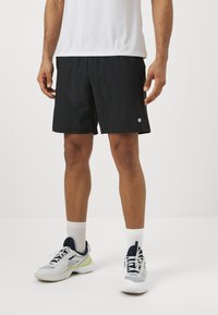 Calções de desporto pretos com uma textura suave, cintura elástica e um pequeno logótipo branco na parte inferior da perna direita. Usados com meias brancas e ténis.