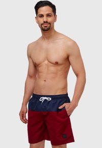 Røde og marineblå badetights med elastisk midje, hvit snøring, sidelommer og et firkantet aksentlogo på venstre bein.
