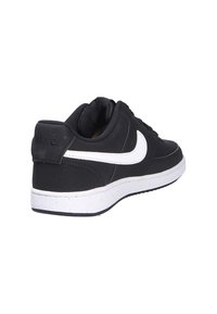 Zapatilla negra de Nike con swoosh blanco, fabricada en material sintético, diseño bajo, superficie texturizada y suela de goma blanca de contraste.