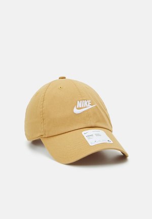 Beige Nike baseballpet met wit geborduurd logo en maatlabel op de klep, afgebeeld tegen een effen lichtgrijze achtergrond.