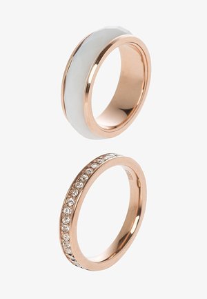 Deux bagues en or rose, l’une avec une incrustation en céramique blanche et l’autre avec une rangée de petits pierres précieuses transparentes autour de l’anneau.