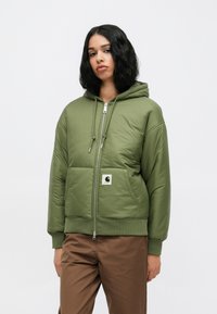 Zelena podložena jakna z zadrgo, kapuco na zategovanje in logotipom. Ima ribane manšete in rob, gladko teksturo in sproščen kroj.