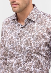 Camicia aderente bianca con un motivo paisley marrone e blu, dotata di colletto a punta e bottoni marroni sul davanti.