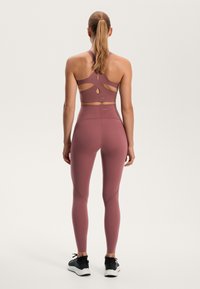 Mauve sportmelltartó kivágott hátrész részletekkel, hozzá illő magas derekú leggingszel párosítva. Sima felület, testhez simuló kialakítás és varratmentes részletek.