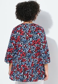 Blusa a stampa leopardata rossa, nera e blu con maniche a tre quarti, orlo arricciato e vestibilità morbida. Tessuto strutturato.