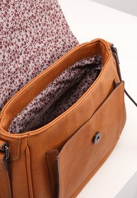 Ruskea nahkainen käsilaukku, jossa on kuvioitu kangasvuori. Varustettu etuläpällä, magneettisuljennalla ja useilla sisätaskuilla.