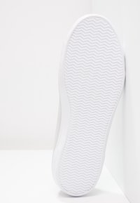 Semelle de chaussure en caoutchouc blanc avec une texture en zigzag, présentant une partie supérieure grise. L'angle met en valeur le design épuré et le contraste des matériaux.