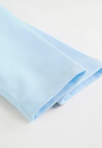 Tissu en coton bleu clair plié avec une texture lisse. Présente un ourlet net et des coutures subtiles le long des bords.