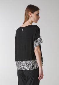 Černý oversize top s krátkými rukávy, zdobený zebrovaným potiskem na lemu a manžetách. Měkká látka s volným střihem.