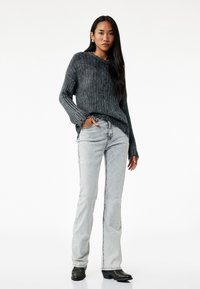 Oversized, geribbelde, donkergrijze trui met lange mouwen, gecombineerd met lichtgrijze, flair jeans en zwarte enkellaarsjes. Zon smooth textuur, casual stijl.