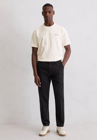Kremowy t-shirt z krótkim rękawem i logo, zestawiony z czarnymi, dopasowanymi spodniami i kremowymi trampkami, charakteryzujący się gładką fakturą i casualowym designem.