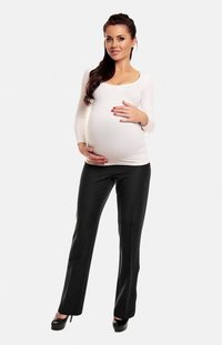 Haut de maternité en tissu blanc avec des manches longues, associé à un pantalon noir ajusté. Le sujet pose avec les mains sur un ventre visible.