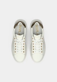 Hvite sneakers med gulløyler og snører. Har en strukturert lysebrun aksent på hælen og en logo trykket i gull på tungen.