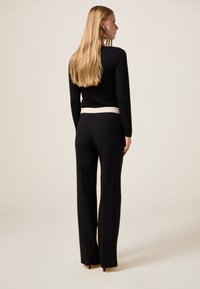 Zwarte top met lange mouwen en een ronde halslijn, gecombineerd met zwarte high-waisted broek met een contrasterende witte tailleband.