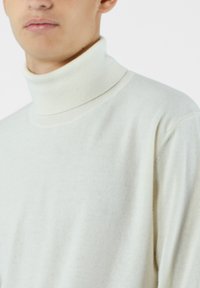 Sweter z golfem w jasnym kremowym kolorze, miękka tekstura, ryżowy kołnierz i mankiety, klasyczny krój, minimalistyczny design bez wzorów czy akcentów.