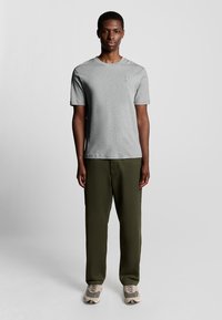 Grå bomulds-t-shirt med korte ærmer, rund halsudskæring og lille logo på brystet, kombineret med olivengrønne løse bukser og lyse sneakers.