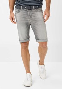 Shorts en denim gris avec revers, accompagnés d'une ceinture texturée gris. Portés avec des baskets blanches sur un fond uni.